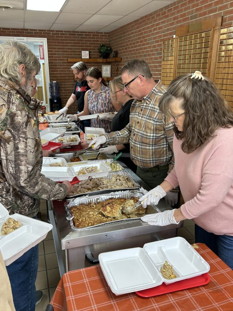 Volunteers in aprons and gloves serving food along the buffet line