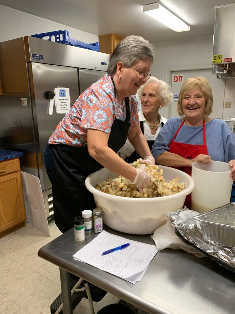 Two smiling volunteers mixing stuffing in a large bowl