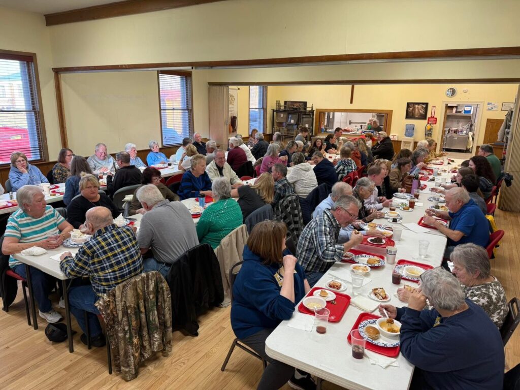 Full Fellowship Hall with guests seated at tables sharing a meal
