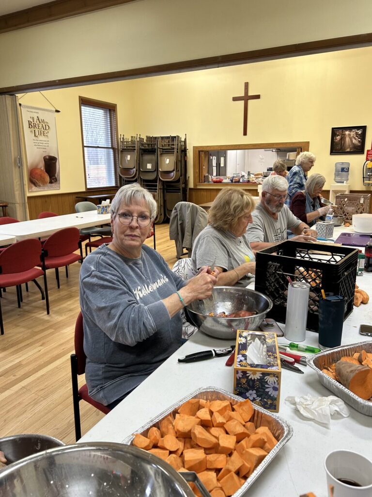 Volunteers at Fellowship Hall tables peeling and cubing sweet potatoes