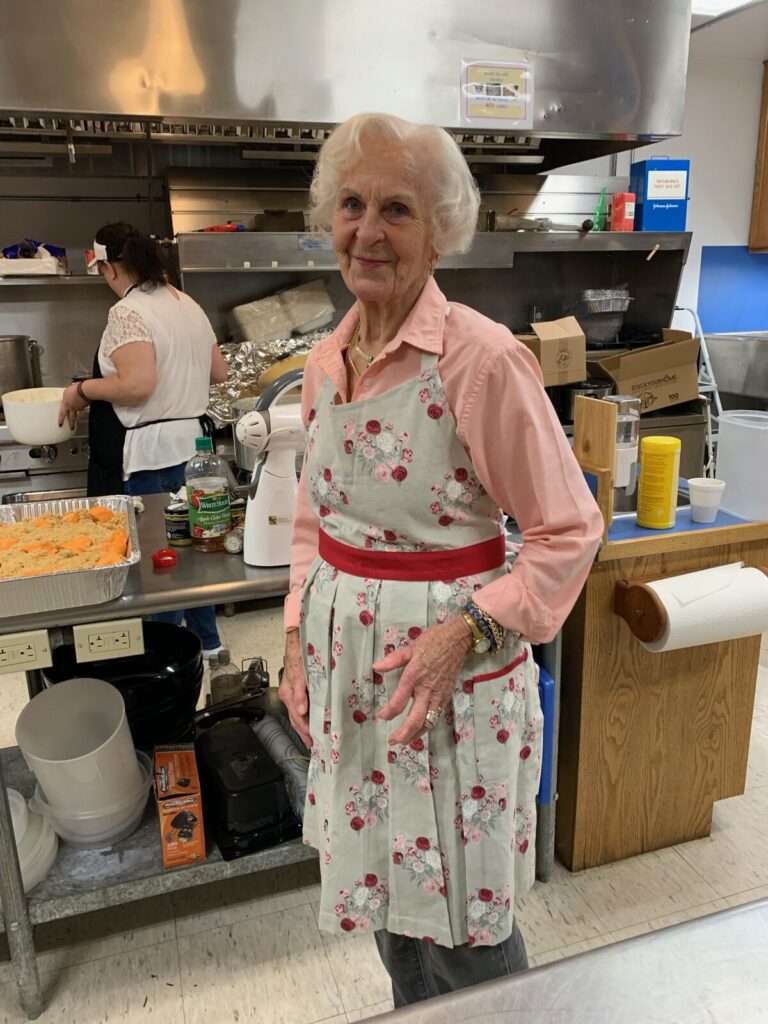Smiling volunteer in a floral apron standing in the church kitchen