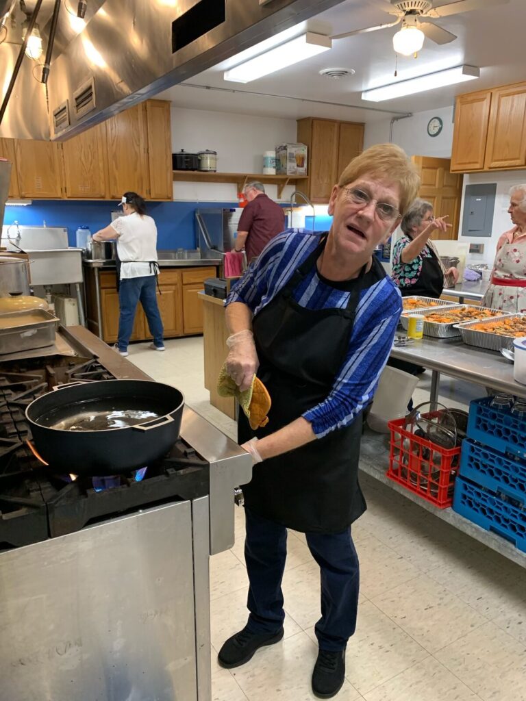 Volunteer in a black apron cooking at the stove in the church kitchen