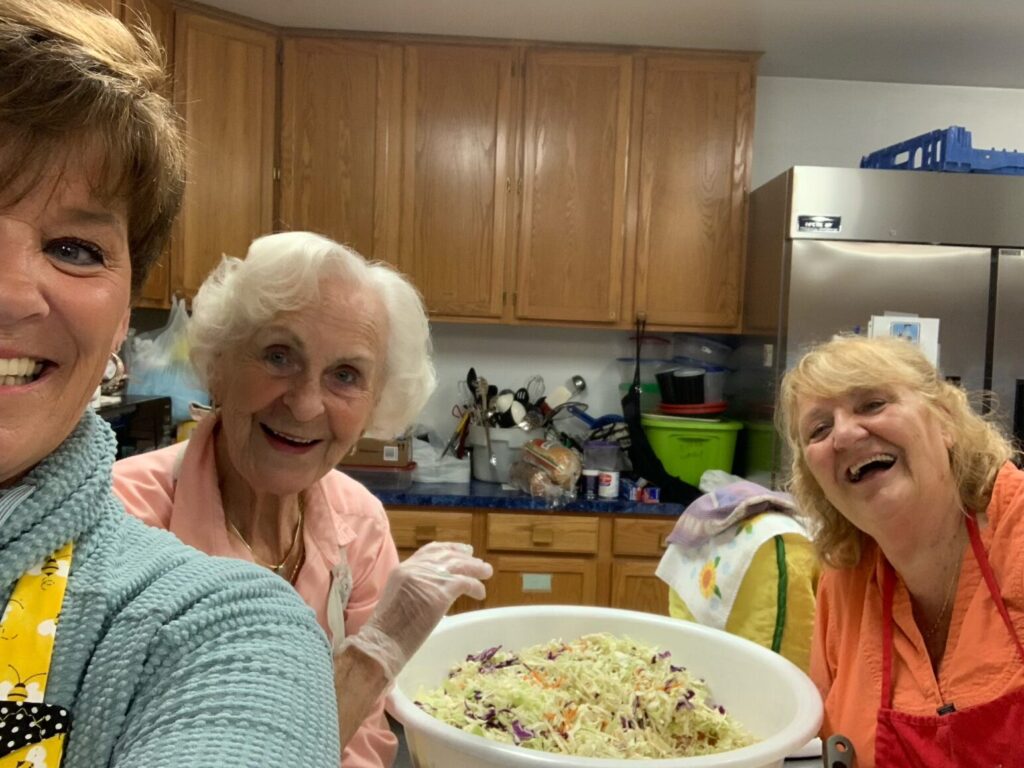 Three laughing volunteers with a large bowl of salad