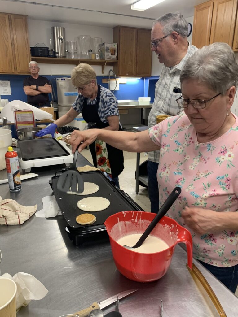 Volunteer pouring pancake batter on a griddle as others cook