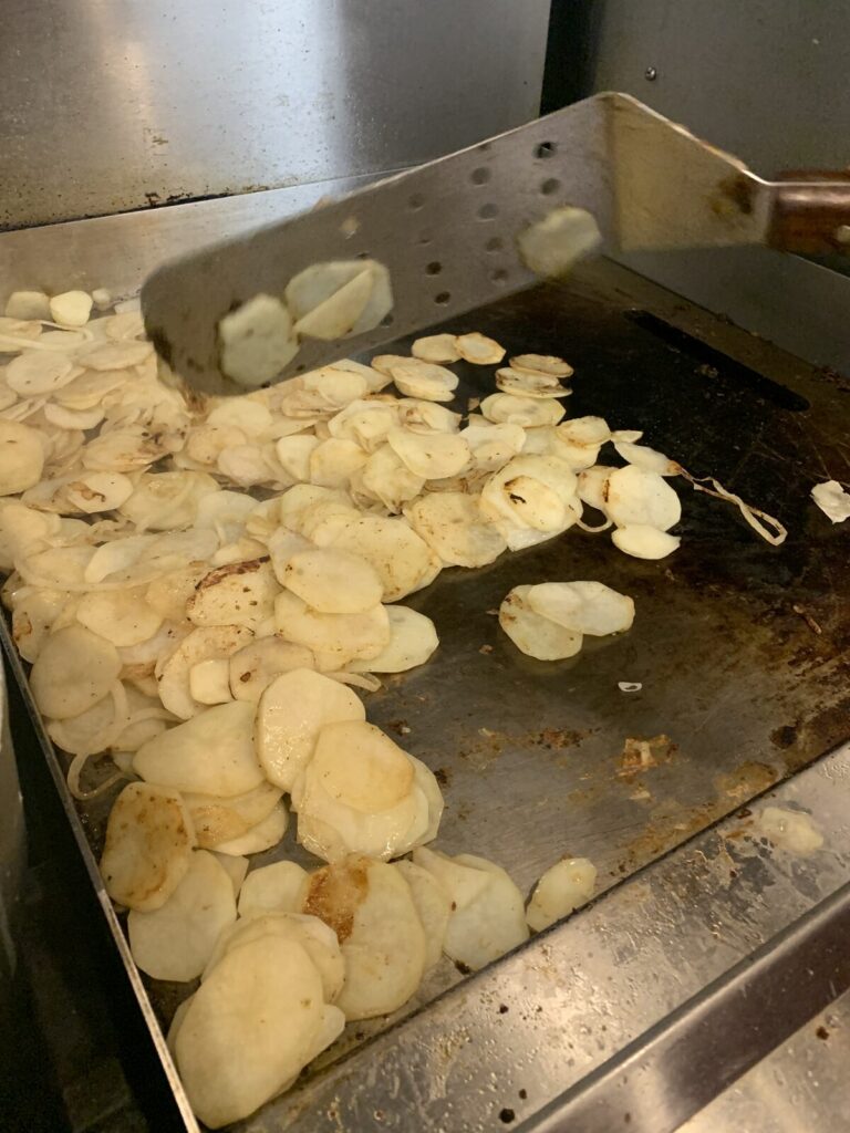 Sliced potatoes frying on the kitchen griddle