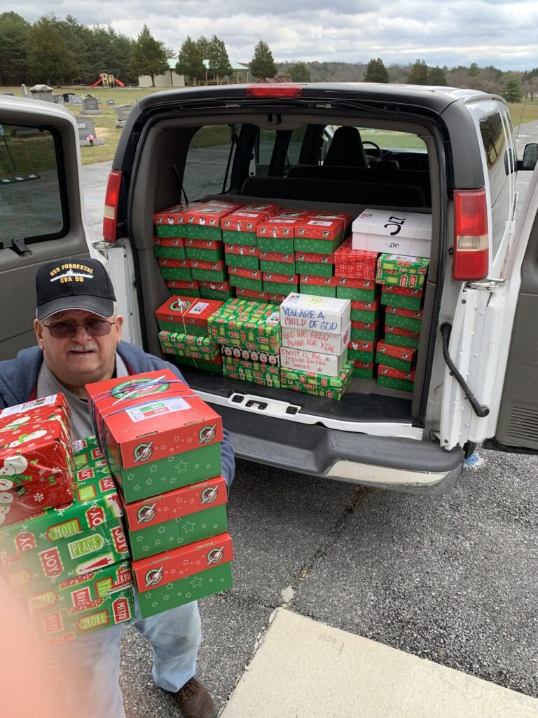 Volunteer carrying a stack of Operation Christmas Child shoeboxes to a van packed full of boxes