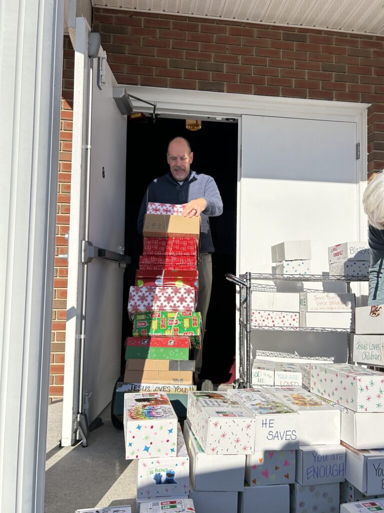 Volunteer wheeling a tall stack of Operation Christmas Child shoeboxes out of the church